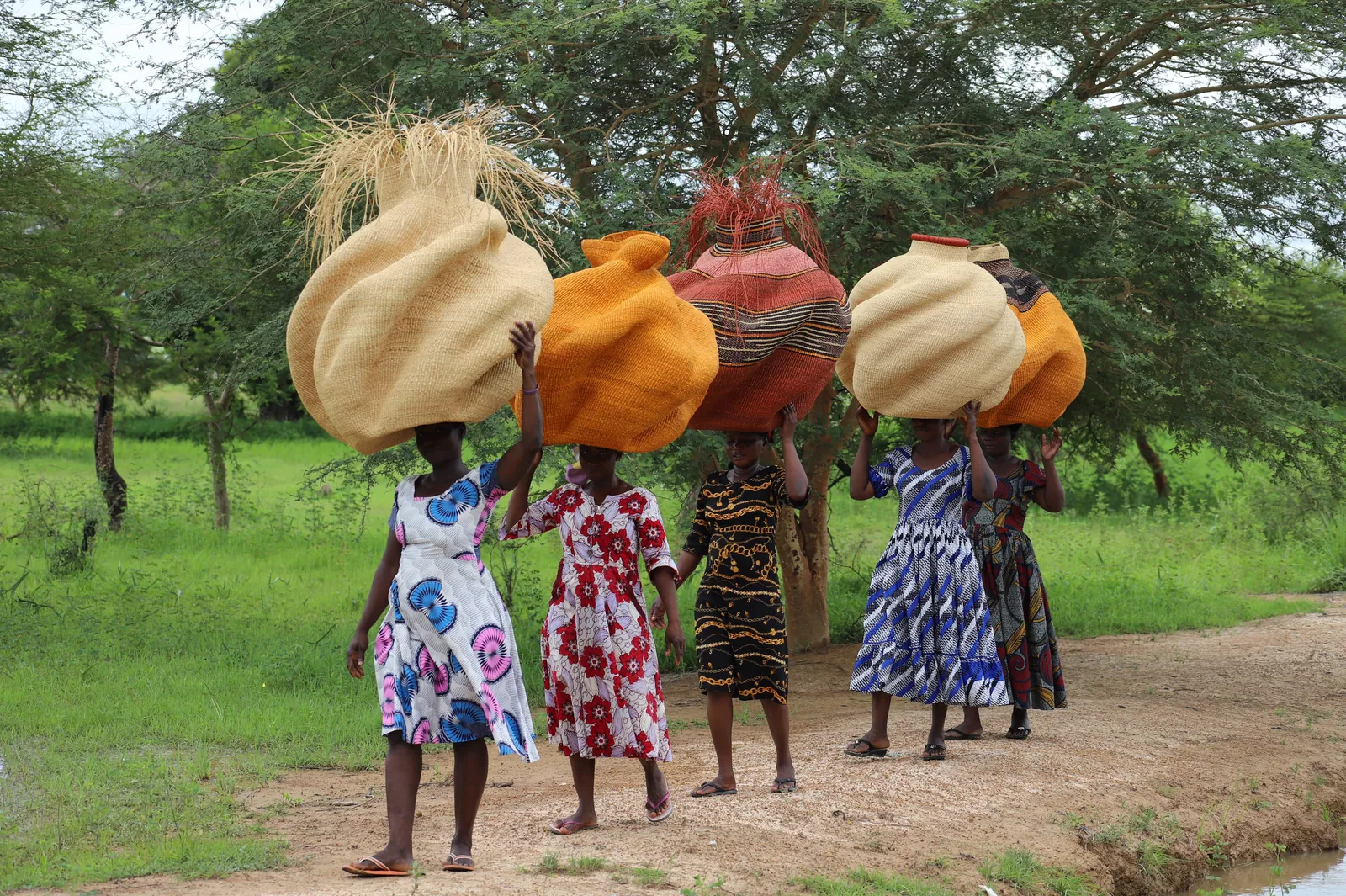 People carrying sculptural baskets along an outdoor path.