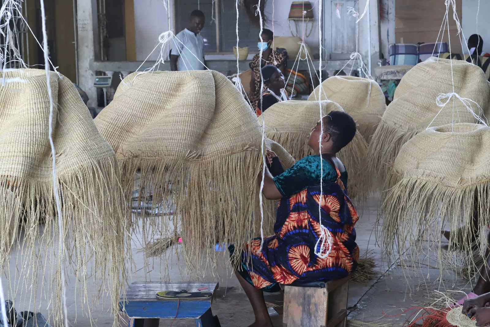A weaver working among large natural-coloured woven lampshades at The Baba Tree compound.