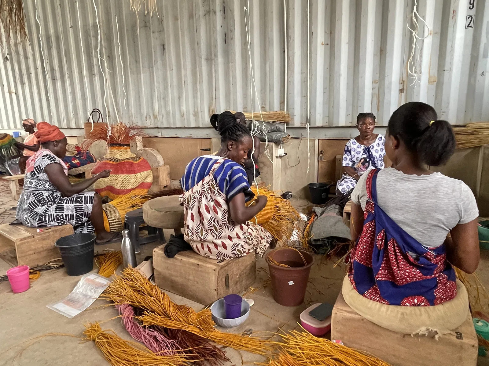 Baba Tree weavers working on baskets together, with straw and woven forms around them.