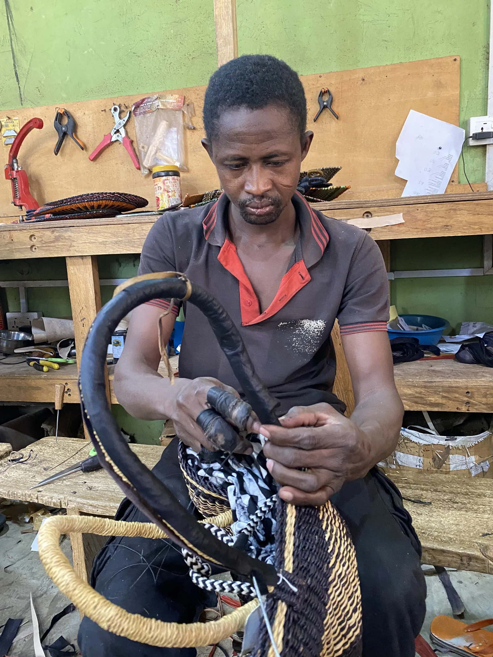 A leather worker lacing a dark leather basket handle at a workbench.