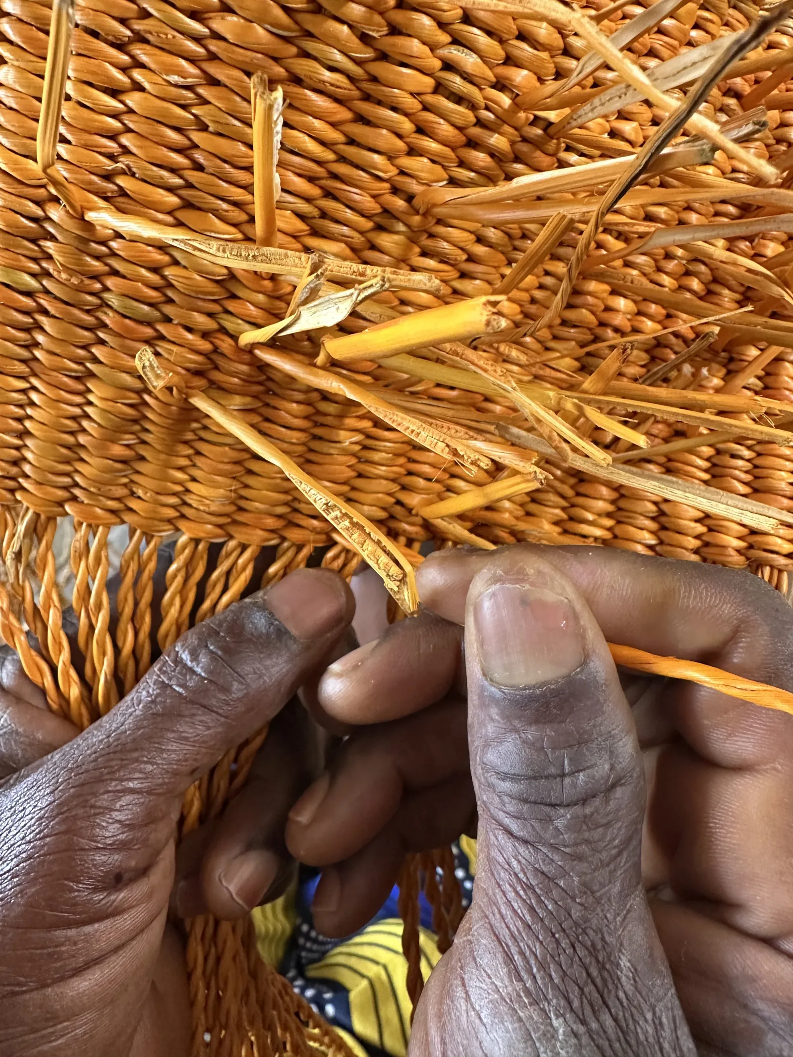 Hands weaving orange straw into a basket, showing the interlaced structure up close.